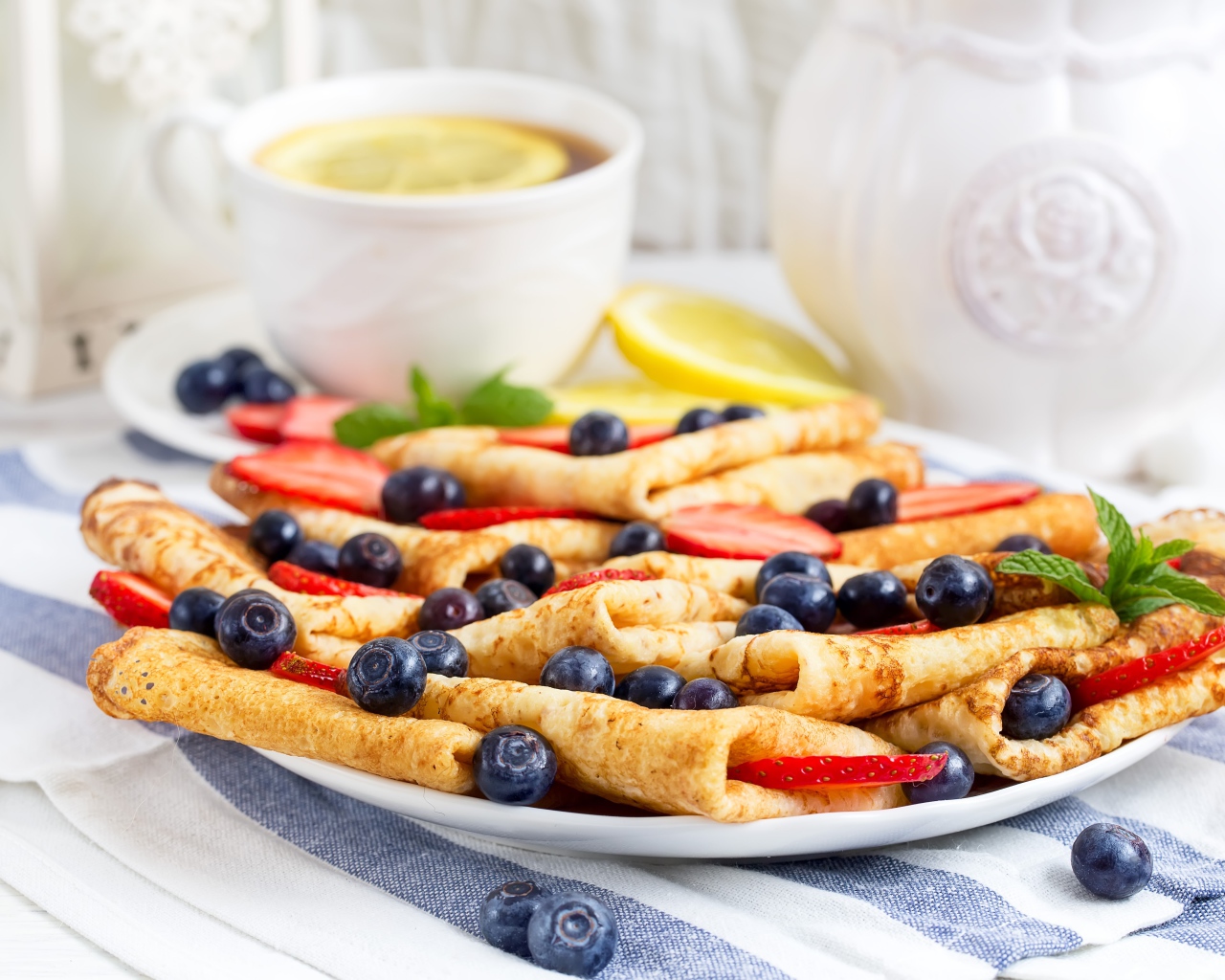 Тонкие блинчики с ягодами черники и клубники на столе с чаем