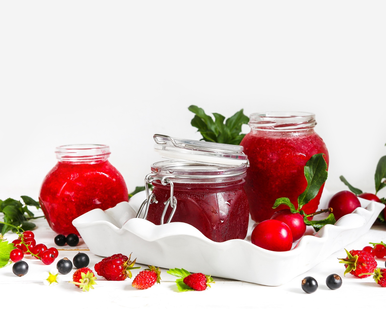 Три банки джема с ягодами на белом фоне