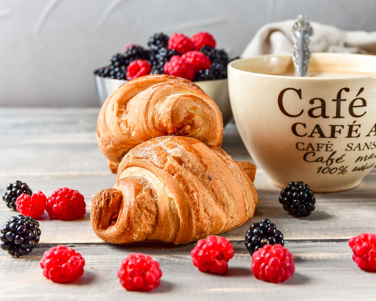 Два круассана с малиной, черникой и чашкой кофе на столе