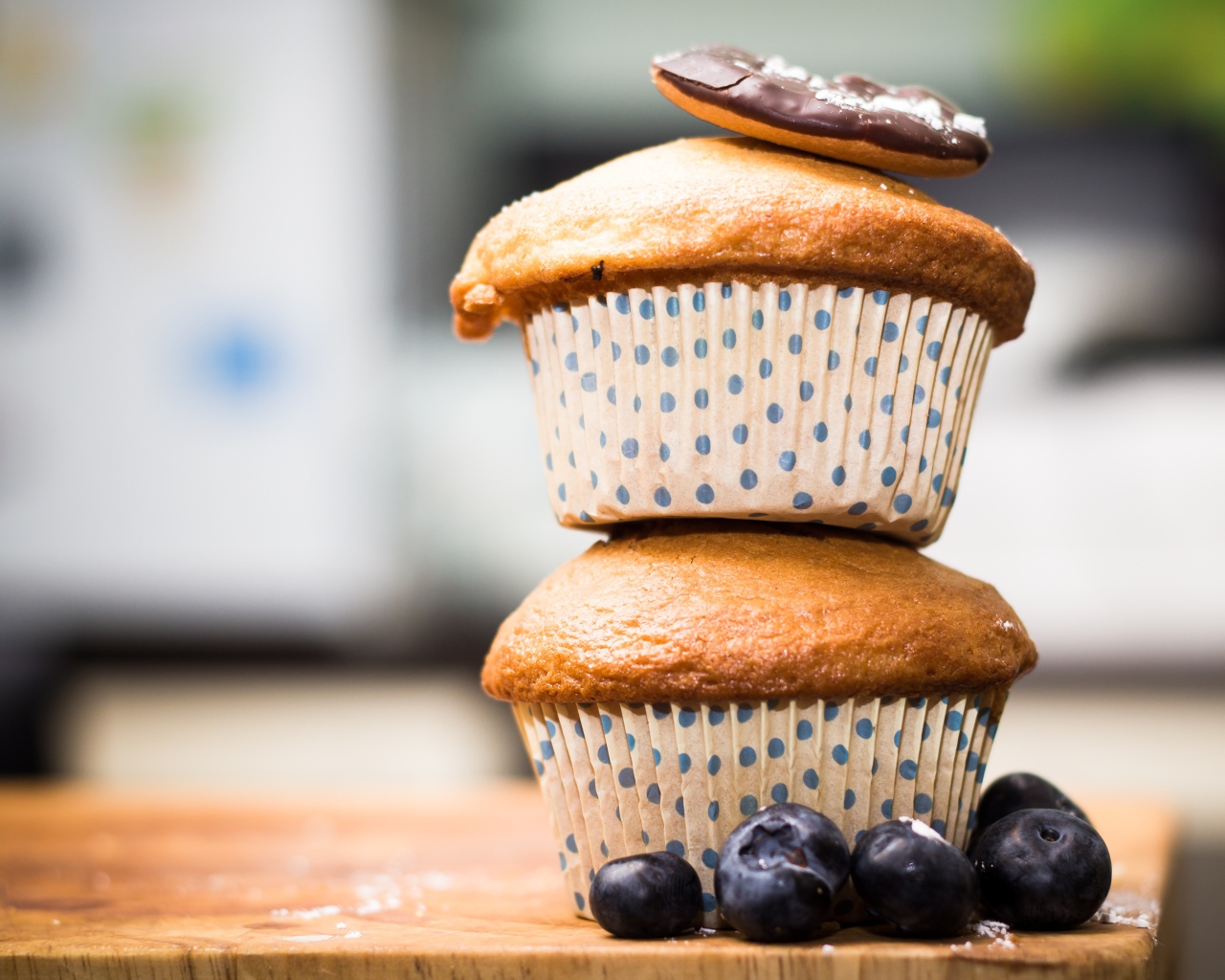 Два кекса стоят на столе с ягодами черники 