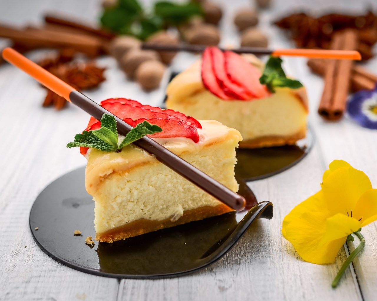 Два куска чизкейка с клубникой на столе с палочками