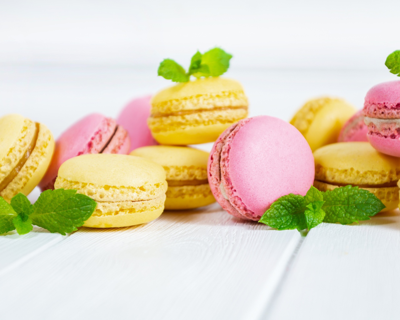 Желтый и розовый десерт макарун на белом фоне с мятой