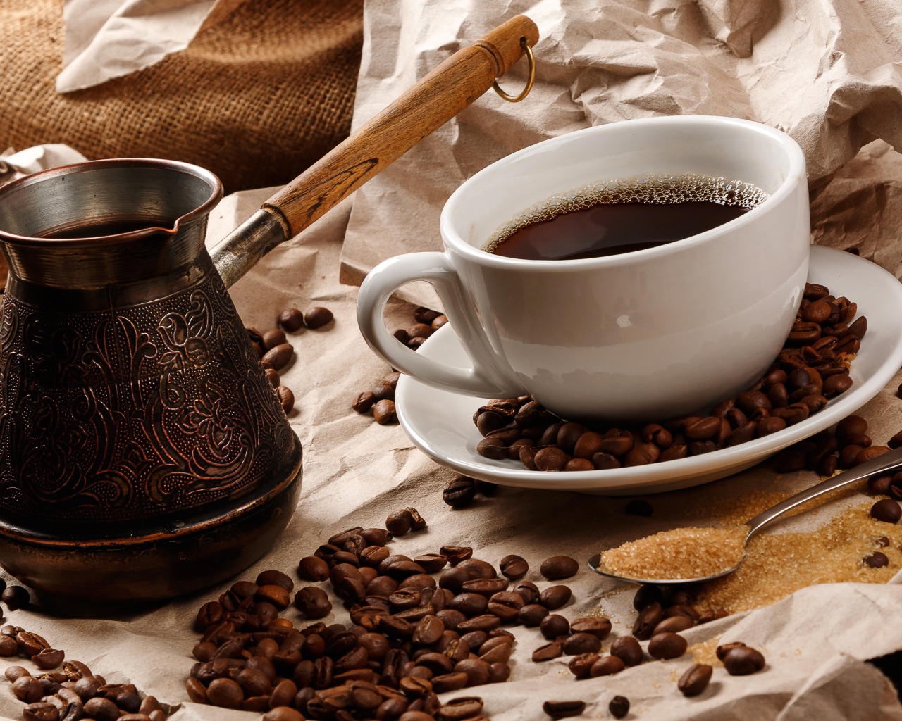 Чашка горячего кофе на столе с туркой, зернами и коричневым сахаром