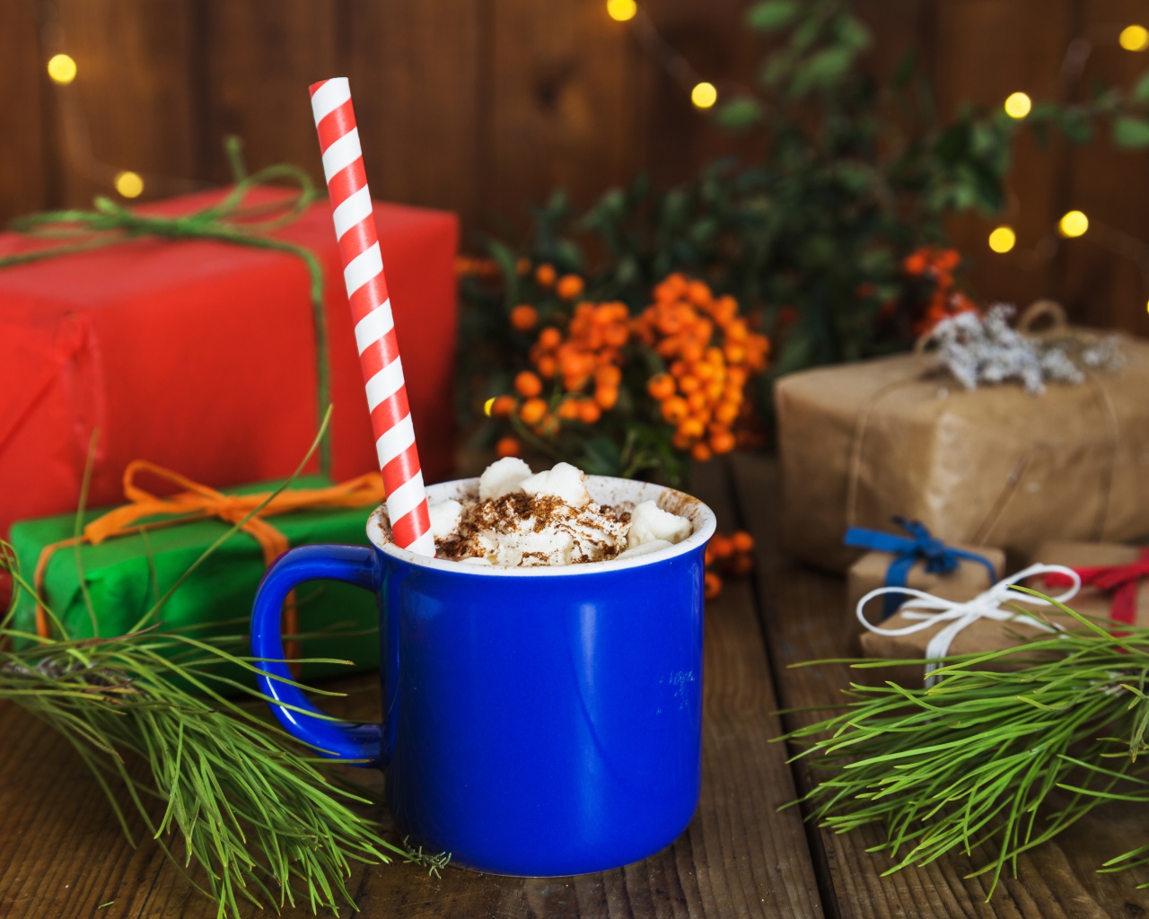 Синяя чашка горячего шоколада с маршмеллоу на столе с еловыми ветками и подарками