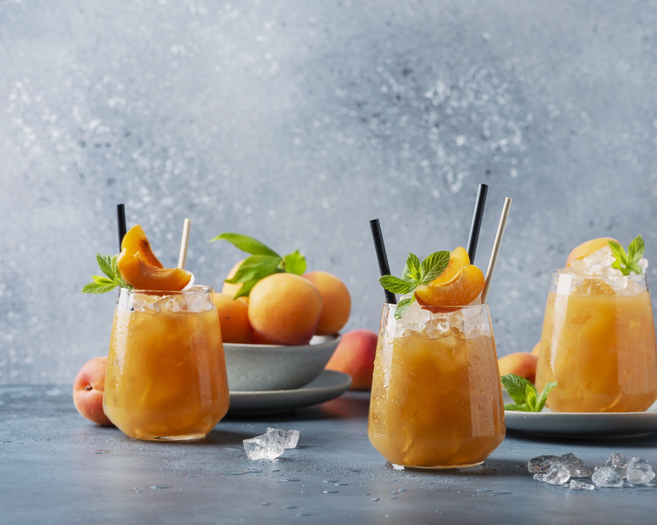Холодный абрикосовый напиток со льдом в стаканах на столе со свежими абрикосами