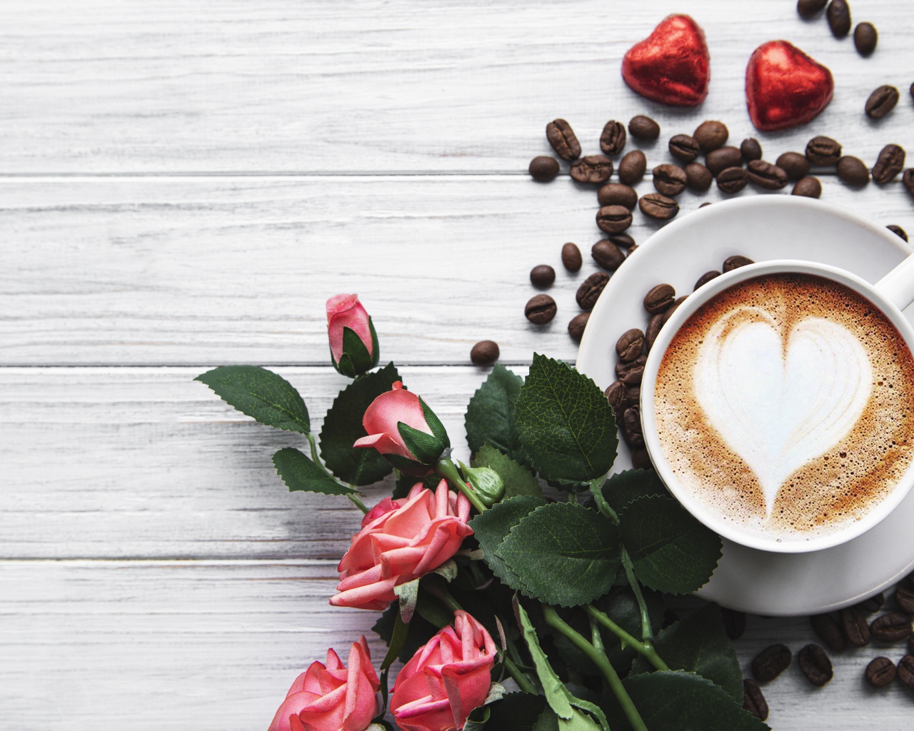 Чашка кофе с рисунком на пене на столе с букетом роз, зернами и конфетами