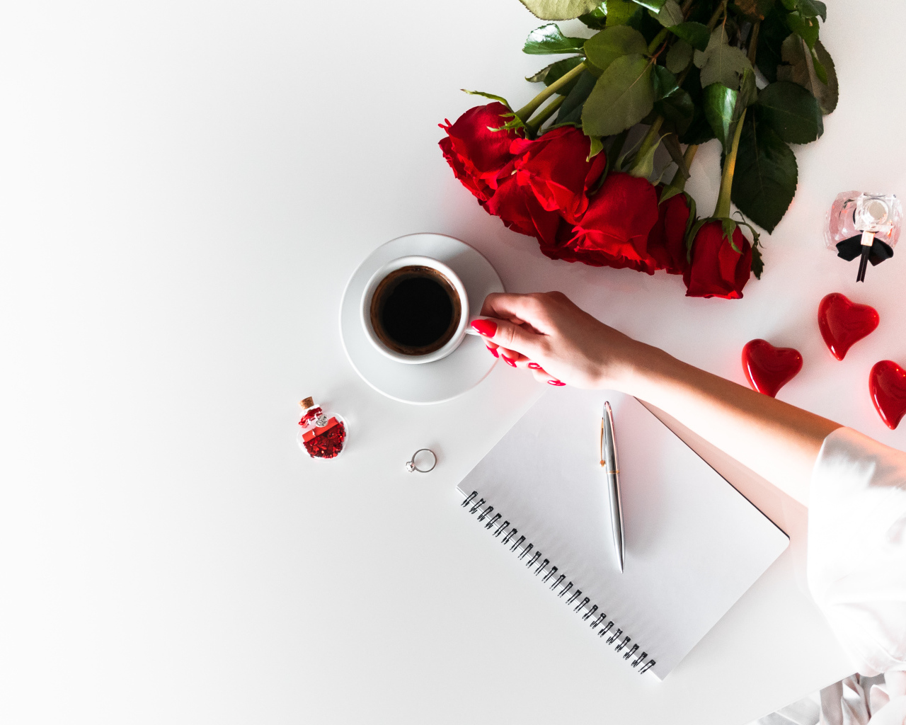 Девушка держит в руках чашку кофе на столе с блокнотом и букетом роз 
