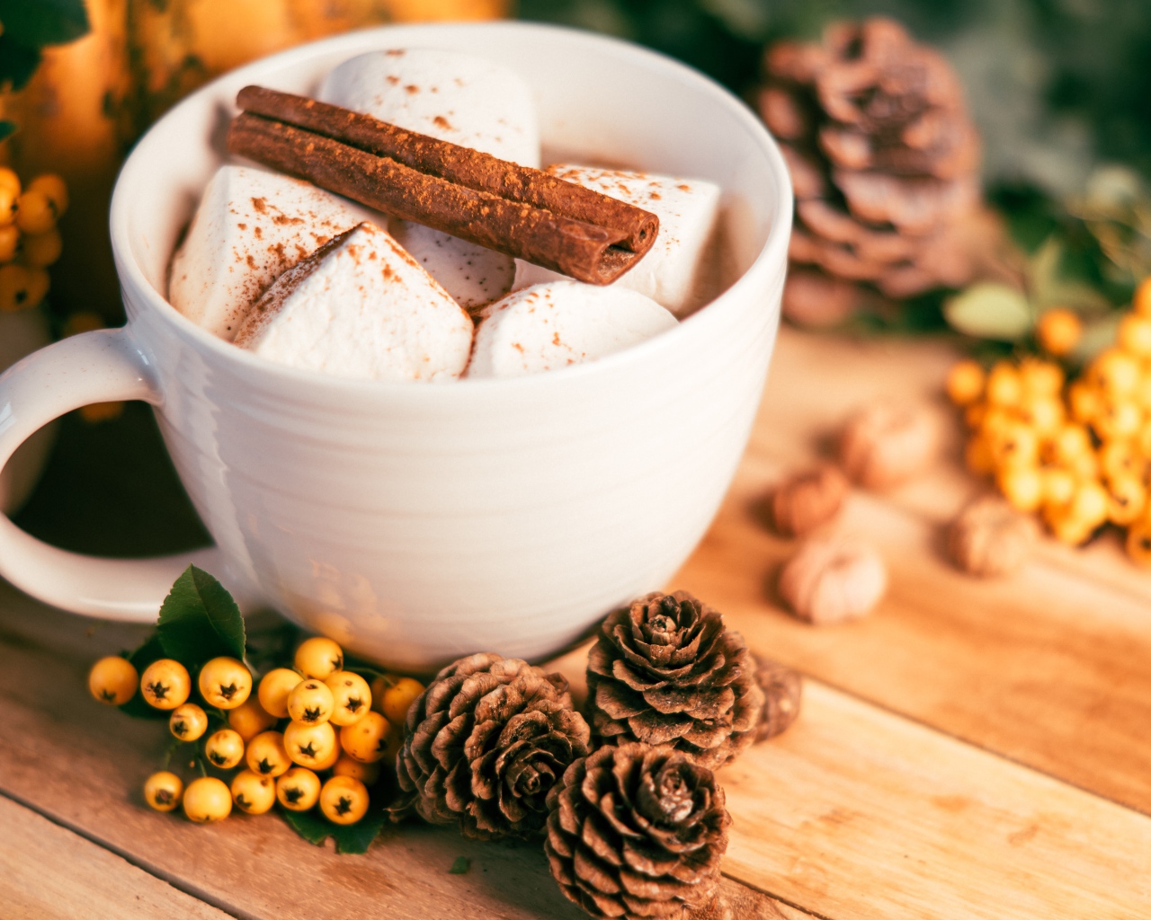 Маршмеллоу в чашке с корицей на столе с шишками и гроздьями рябины