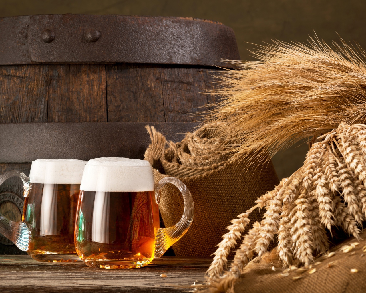 Два бокала пива на столе с колосьями пшеницы  и бочкой