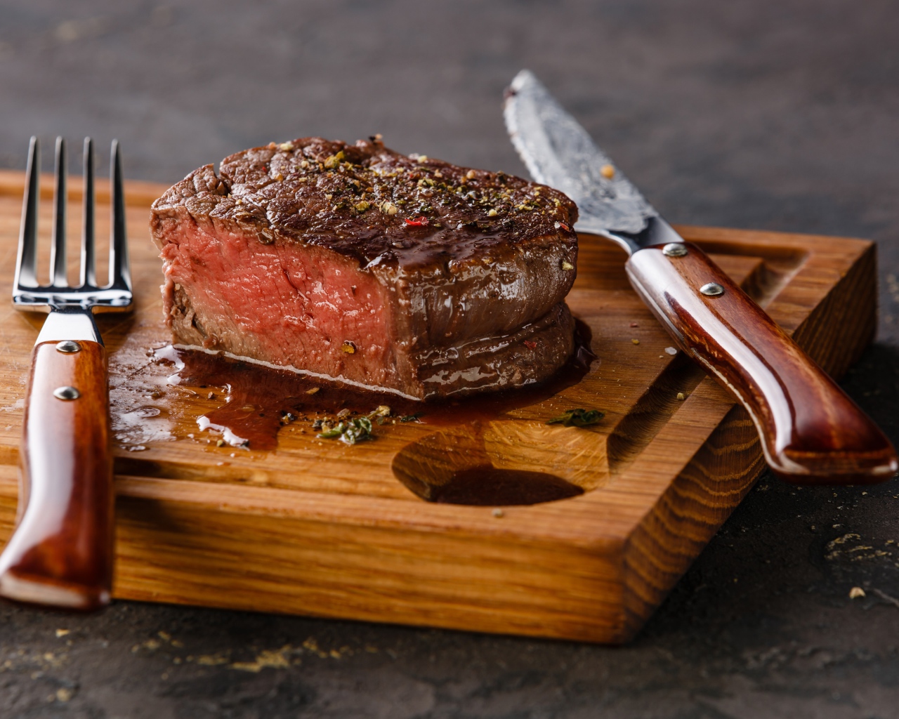 Кусок сочного мяса на доске с ножом и вилкой 