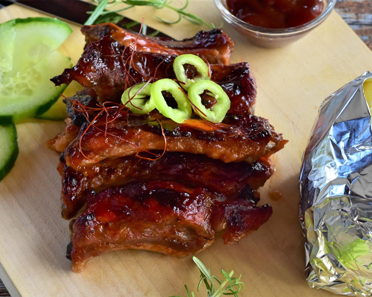 Аппетитные жареные ребрышки на столе с огурцами  и соусом 