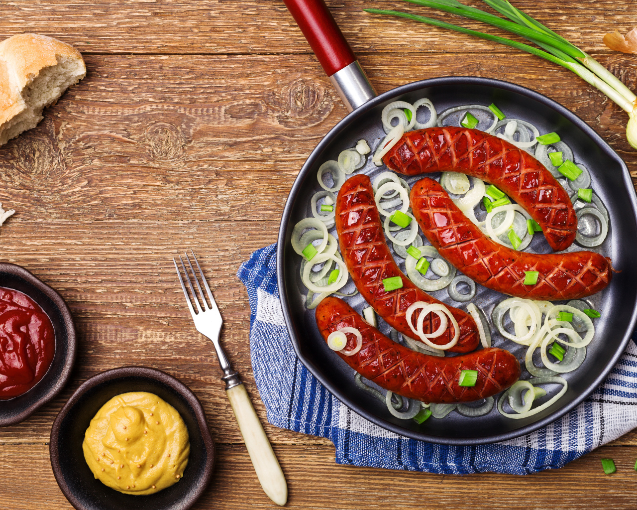 Колбаски барбекю с луком на сковороде на столе с соусом