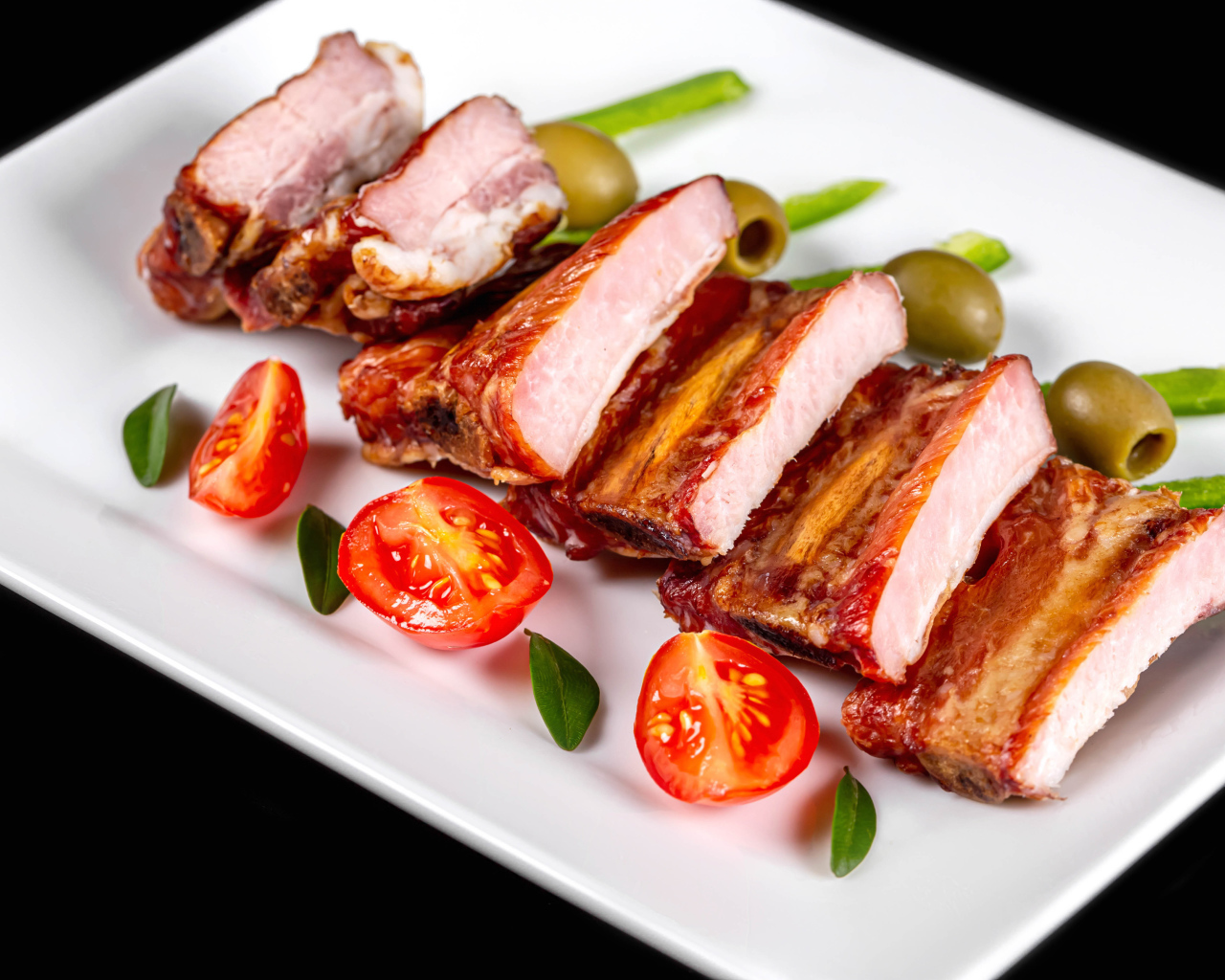 Запеченные ребрышки на белой тарелке с помидорами и оливками