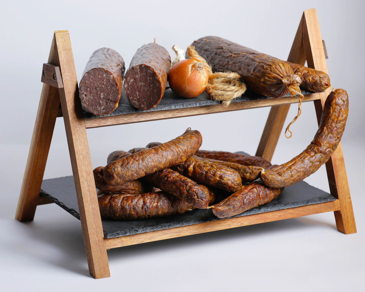Различные виды колбасы на полке с луком на сером фоне