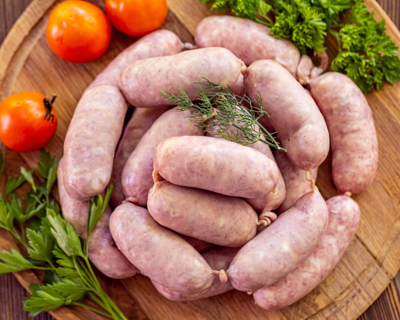 Свежие сырые домашние сардельки на доске с петрушкой и помидорами