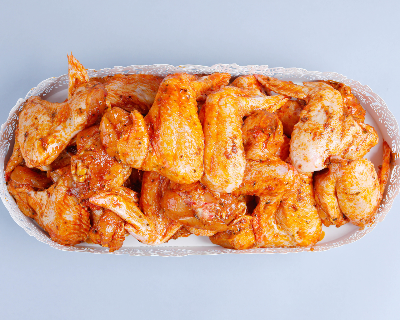 Жареные куриные крылья в белой корзине на сером фоне