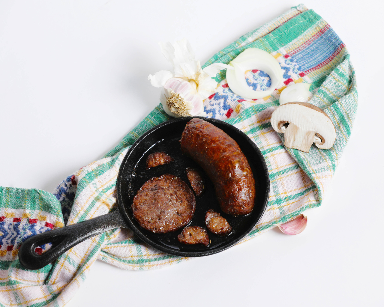 Сковорода с жареной колбасой на столе с полотенцем и чесноком