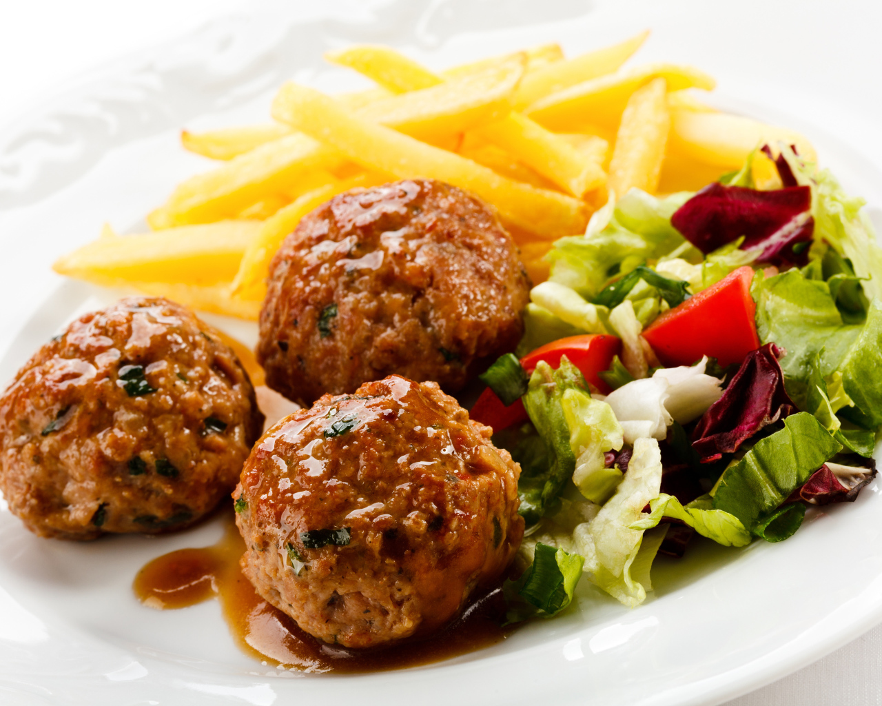 Фрикадельки с салатом и картофелем фри на белой тарелке
