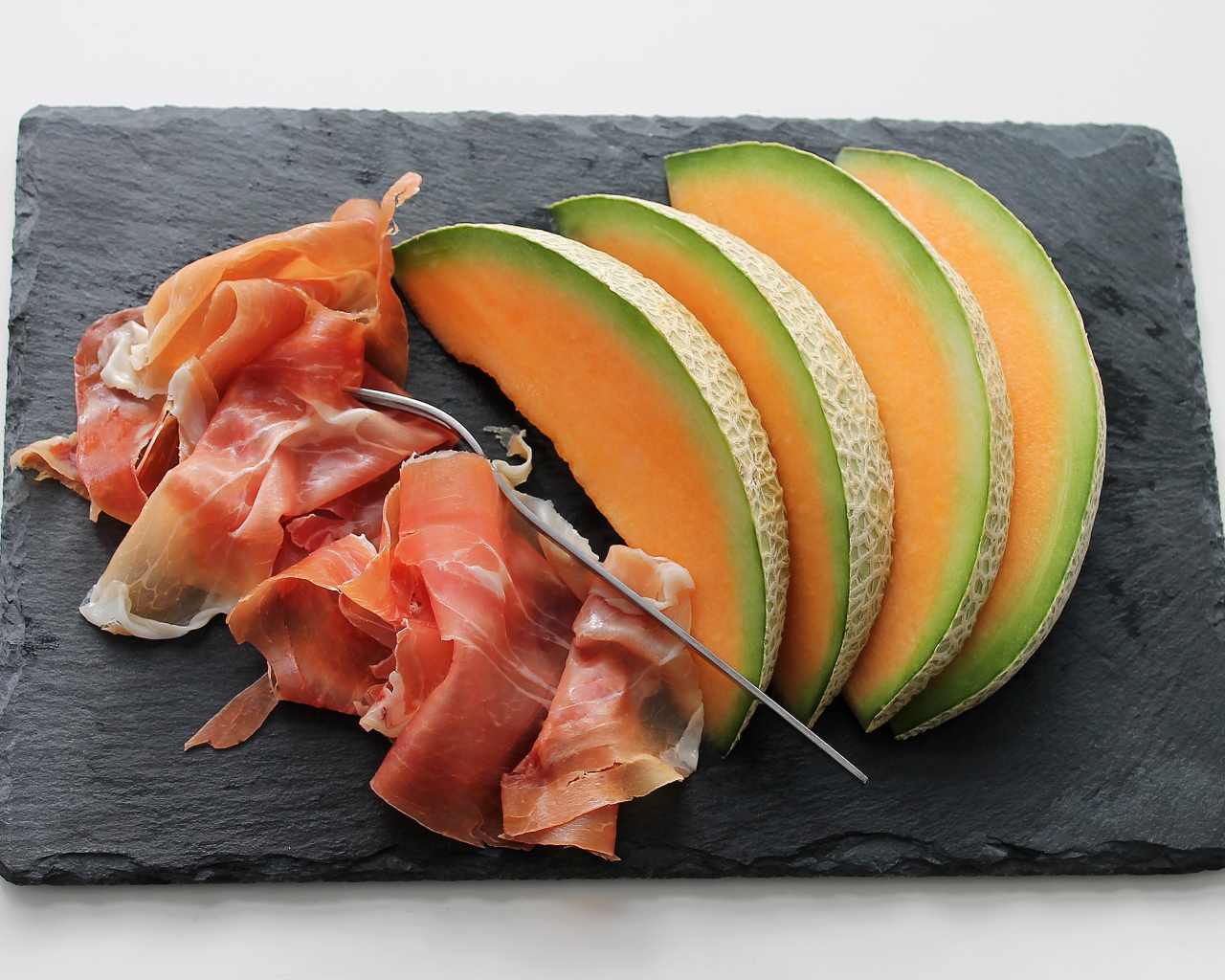 Кусочки дыни на доске с прошутто
