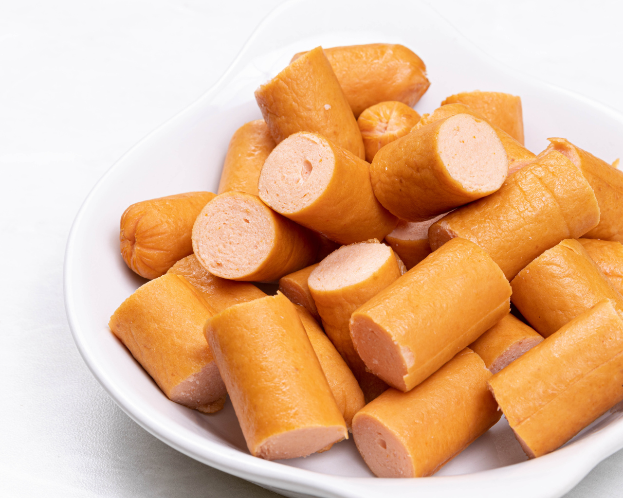 Молочные сосиски кусочками на белом фоне