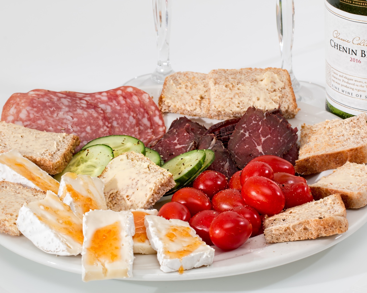 Тарелка с мясными продуктами, яйцами, овощами и хлебом на столе с вином