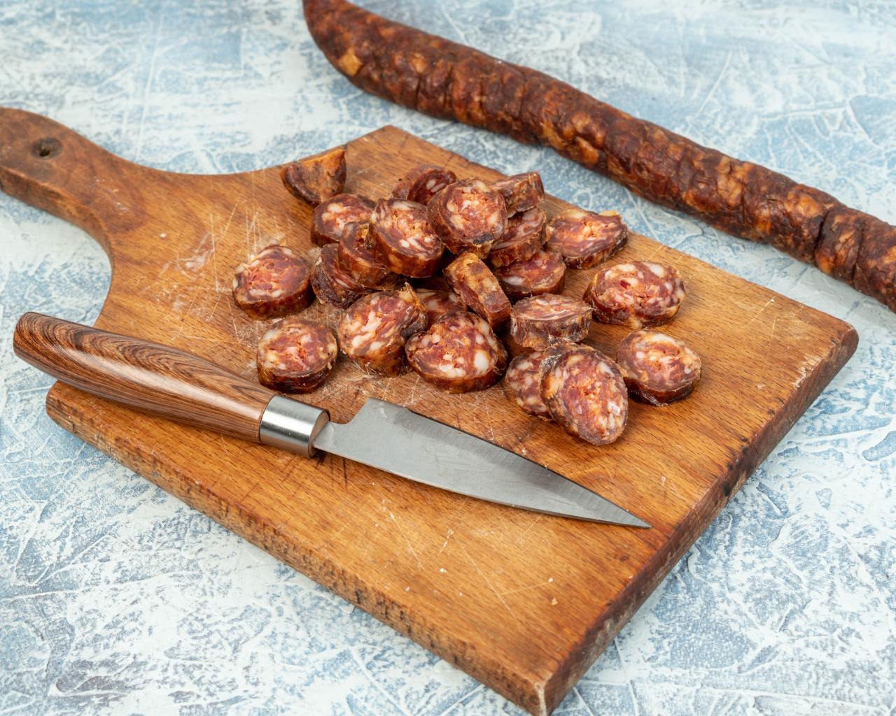 Колбаса нарезана колечками на разделочной доске с ножом 