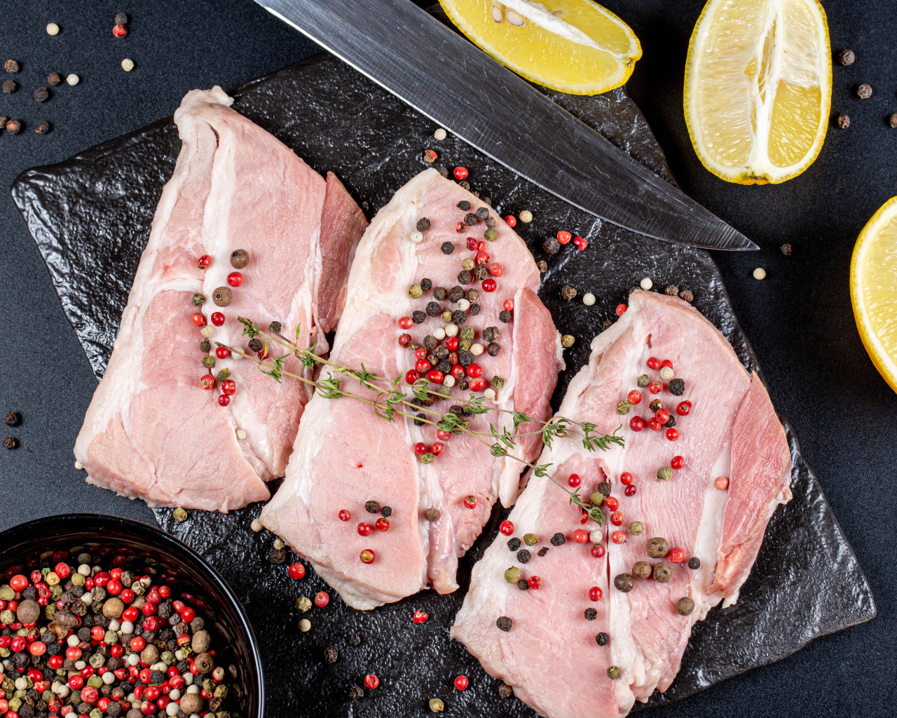 Куски свежего мяса на столе с зернами перца и лимоном