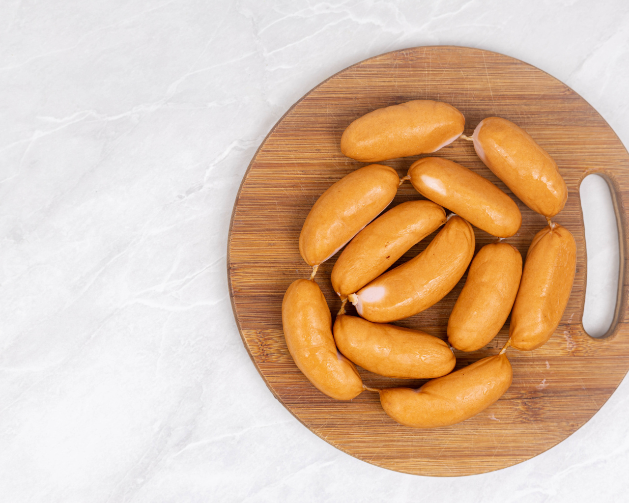 Копченые сардельки на деревянной доске на сером фоне