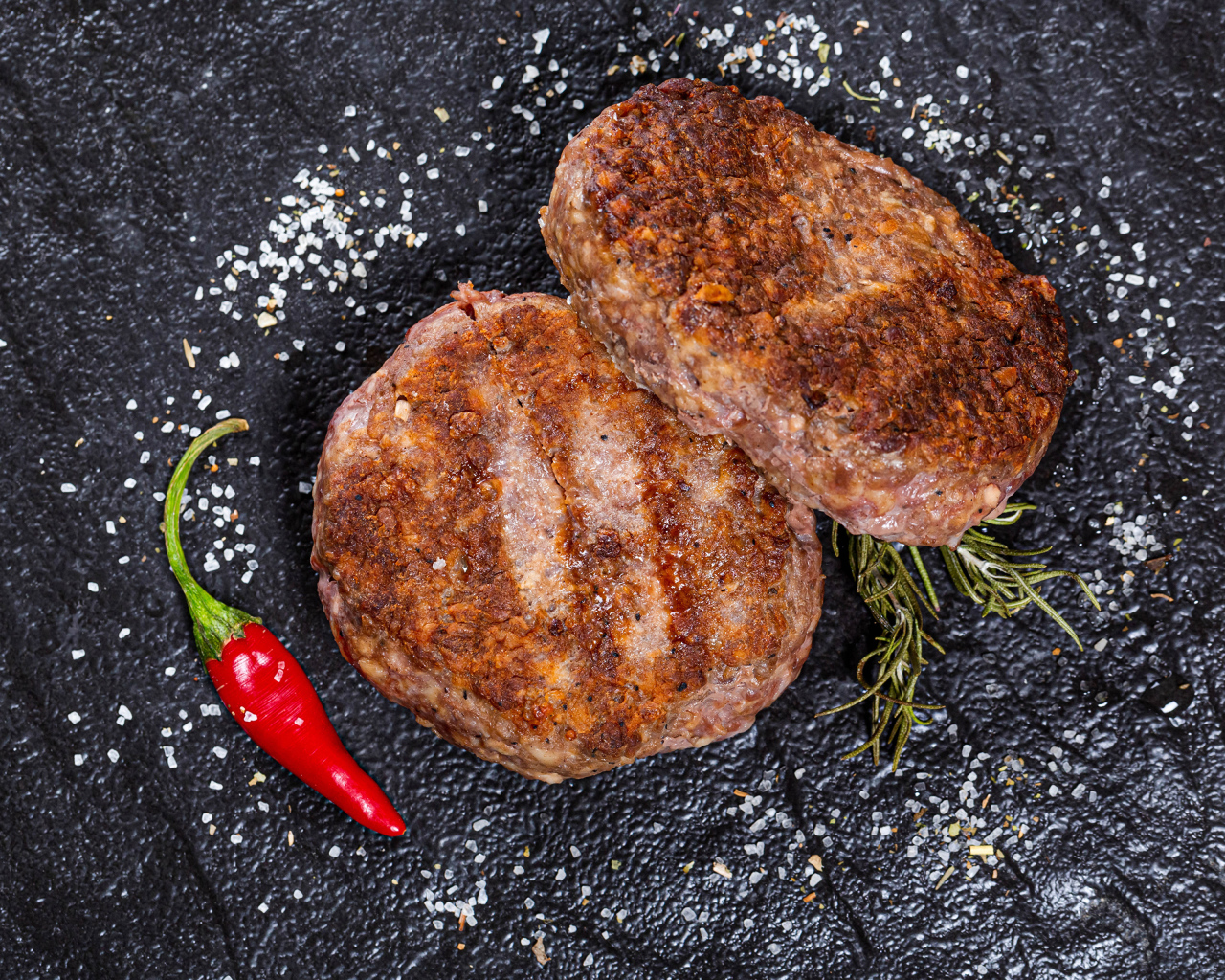 Две котлеты на черной поверхности с красным перцем