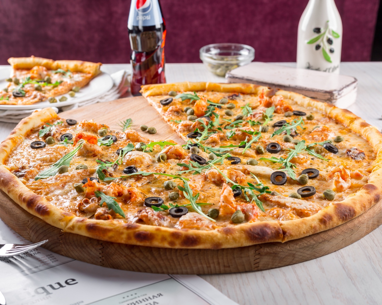 Большая аппетитная пицца с маслинами на столе в кафе