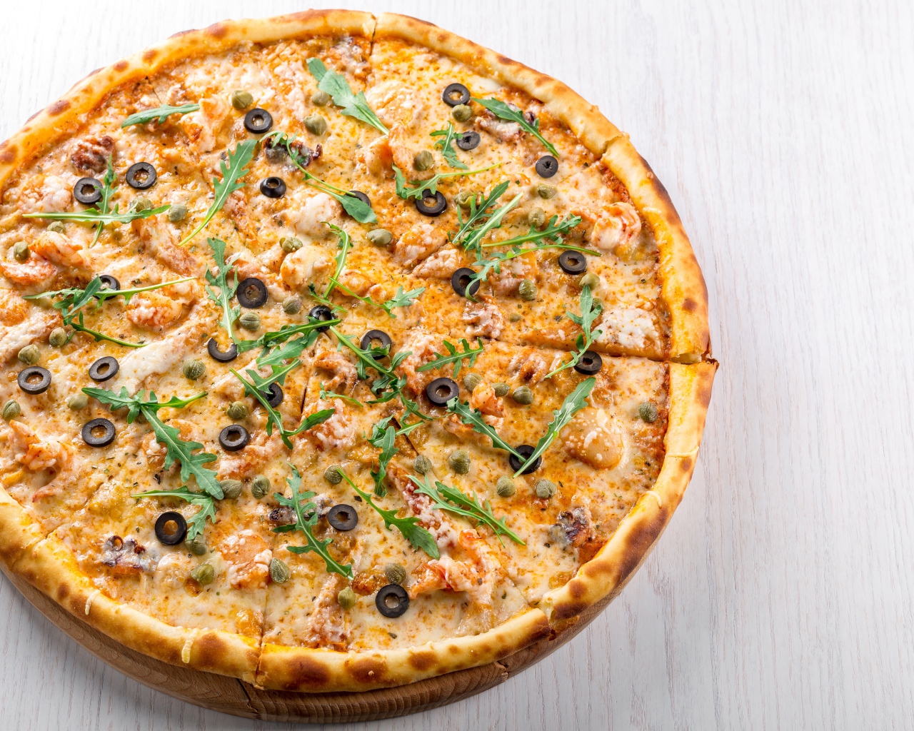 Пицца с морепродуктами, рукколой и оливками на столе 