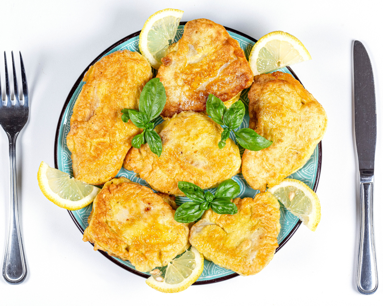 Appetizing fish in batter on a plate with lemon slices and cutlery