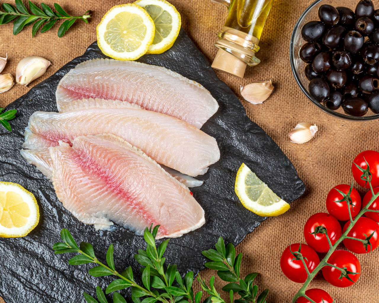Филе рыбы на столе с лимоном, помидорами и оливками