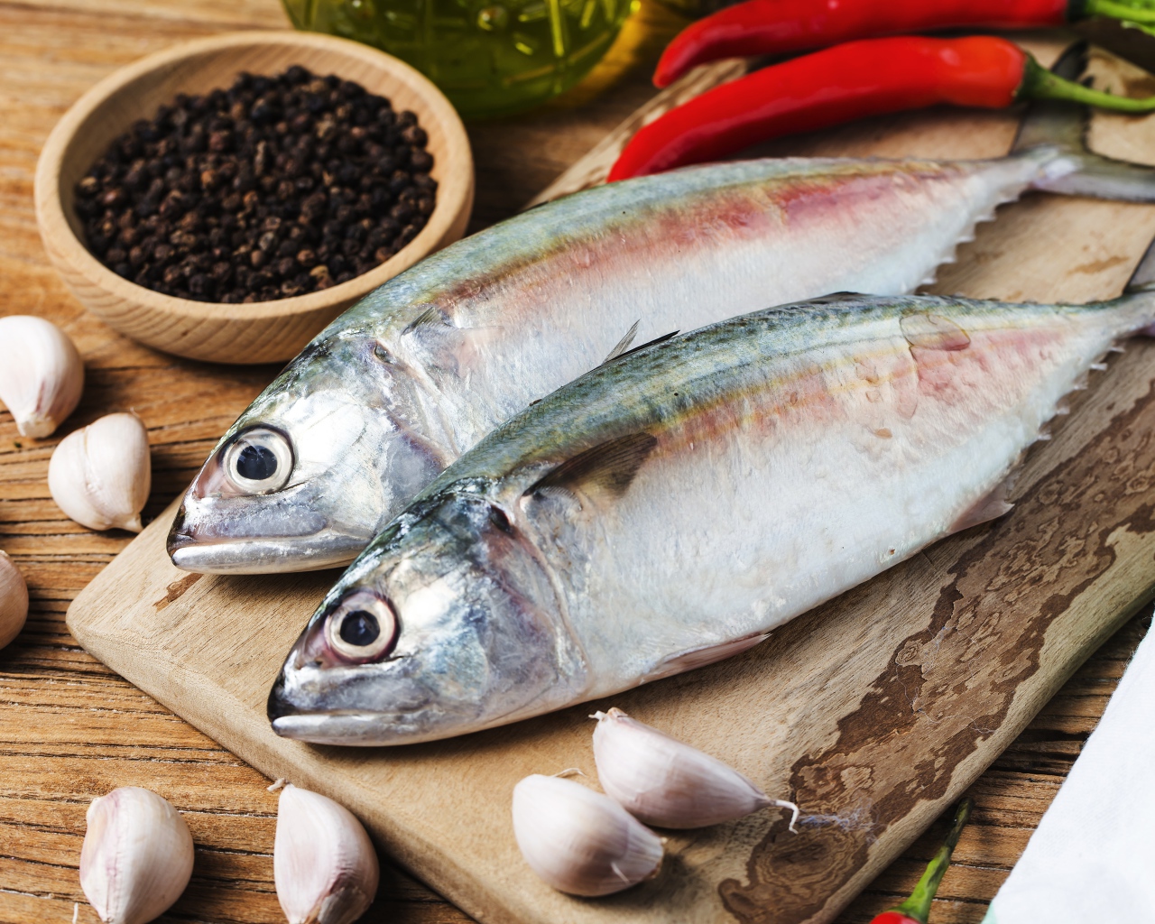 Свежая рыба лежит на доске с чесноком и специями