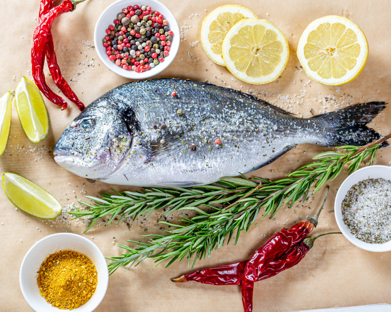 Свежая рыба на столе со специями, лимоном, розмарином и красным перцем