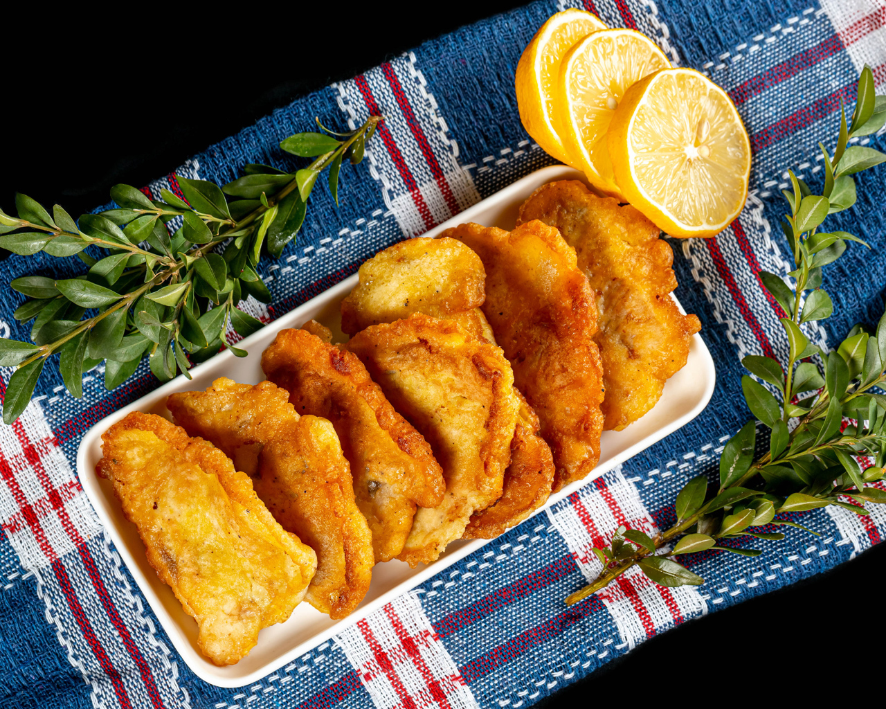 Fried fish in batter on a table with lemon and herbs