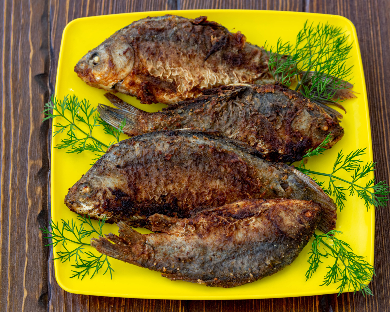 Жареные караси с укропом на желтой тарелке 