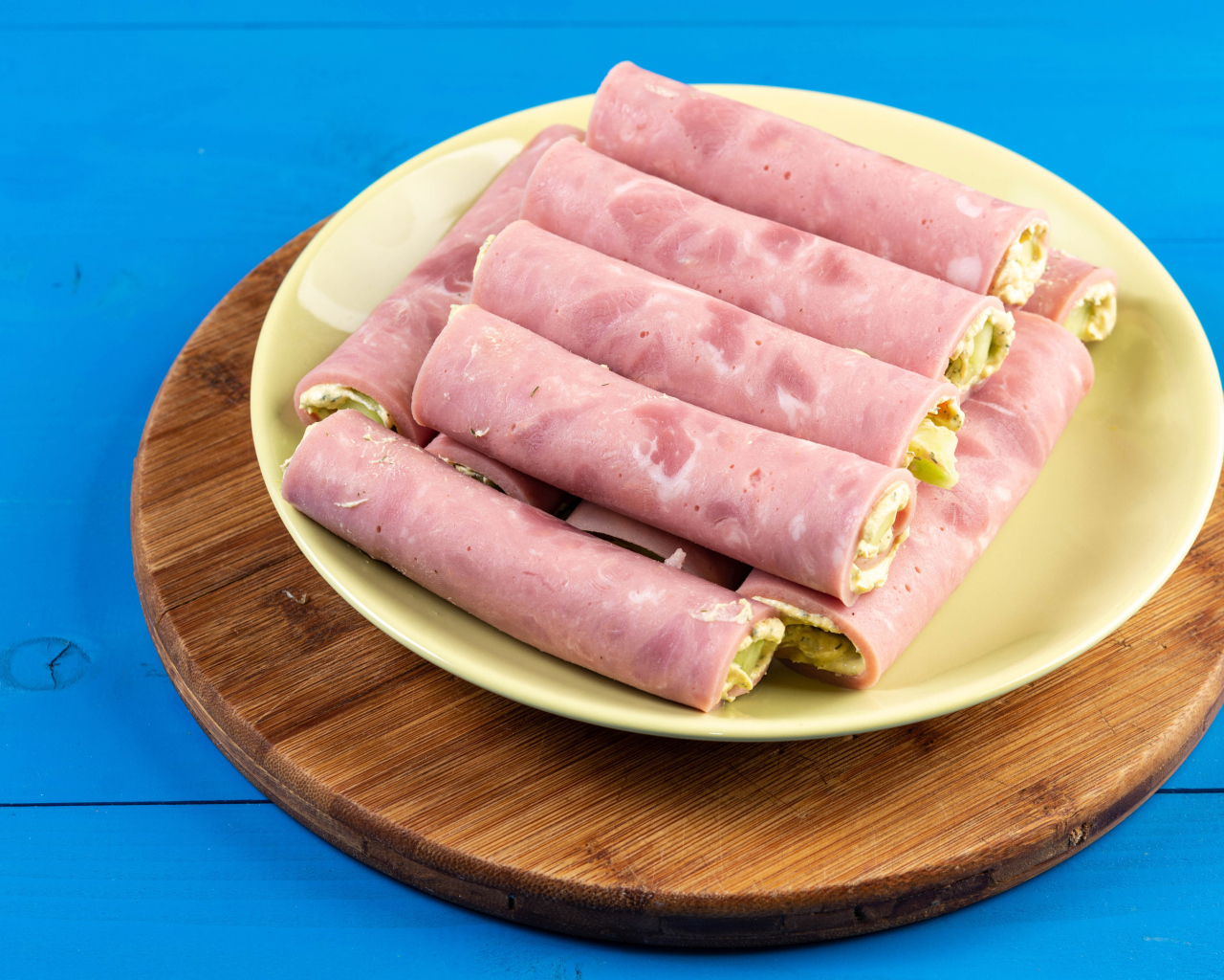 Рулетики из ветчины на тарелке на голубом столе