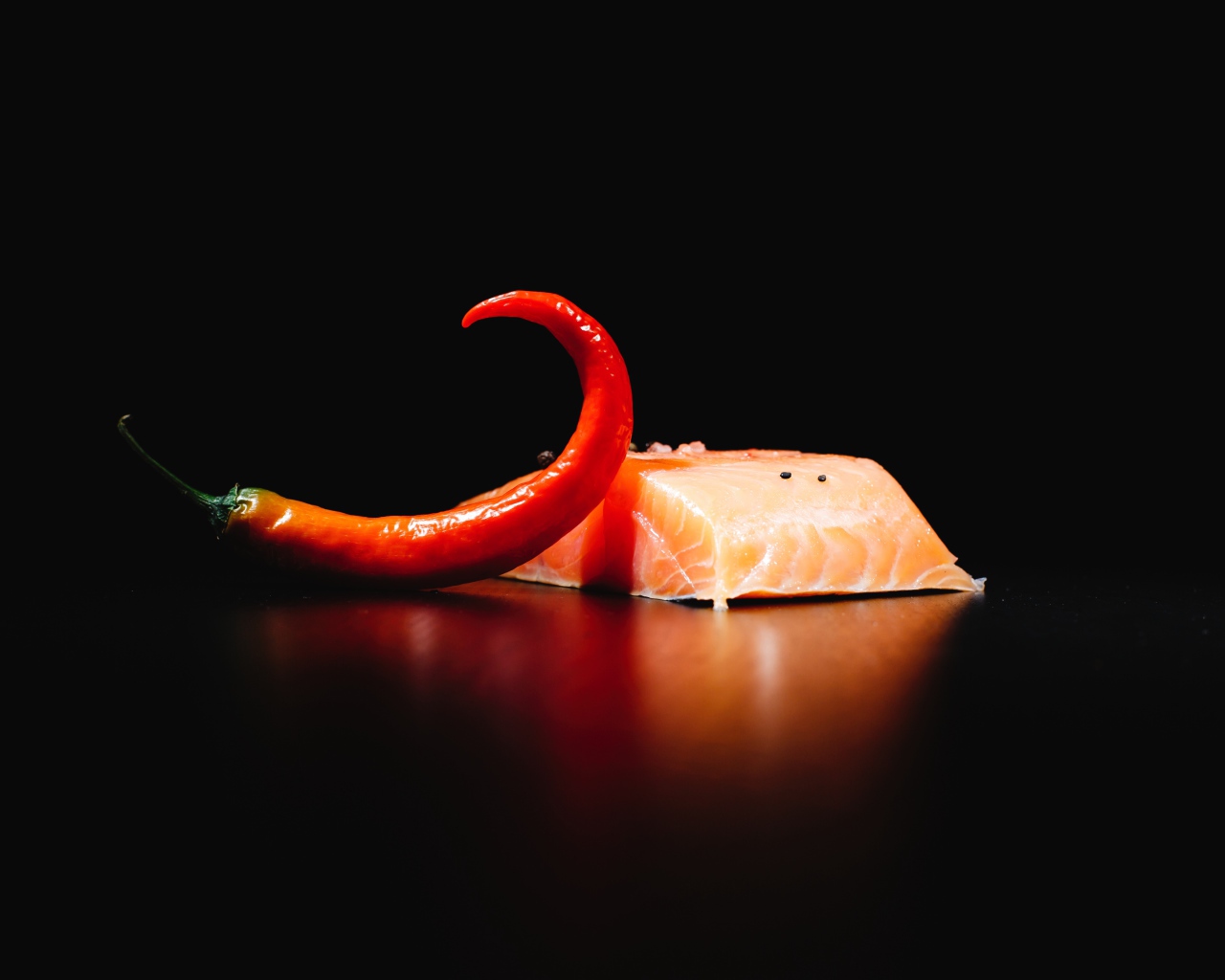 Кусок красной рыбы с острым красным перцем на черном фоне