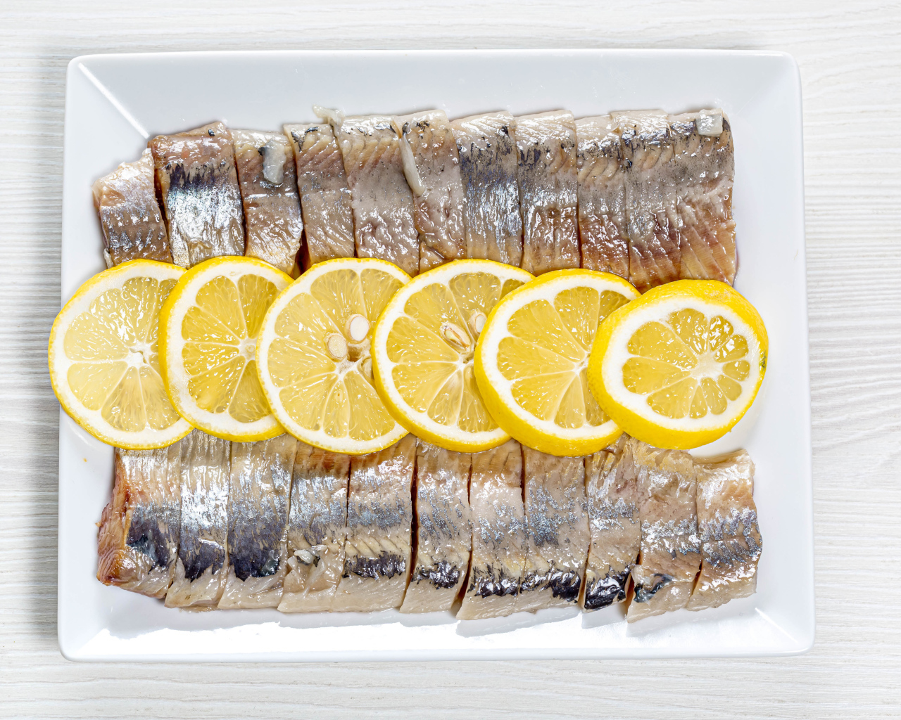 Sliced herring on a white plate with lemon
