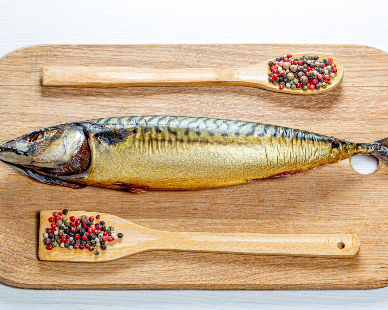 Копченая скумбрия на разделочной доске с перцем на белом фоне