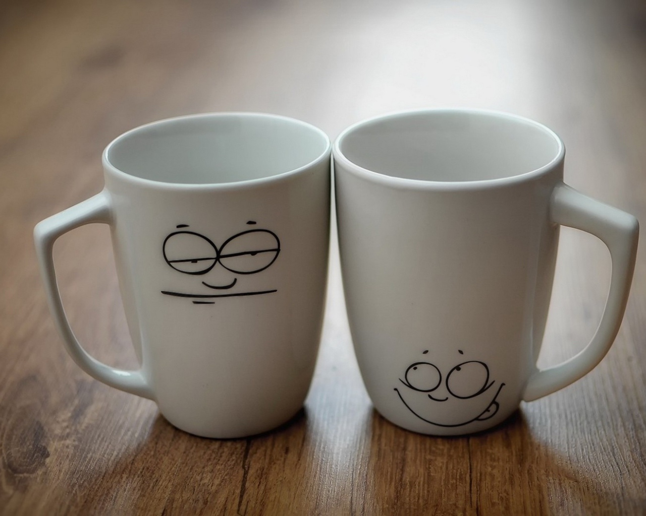 Две белые кружки с рисунками на столе 
