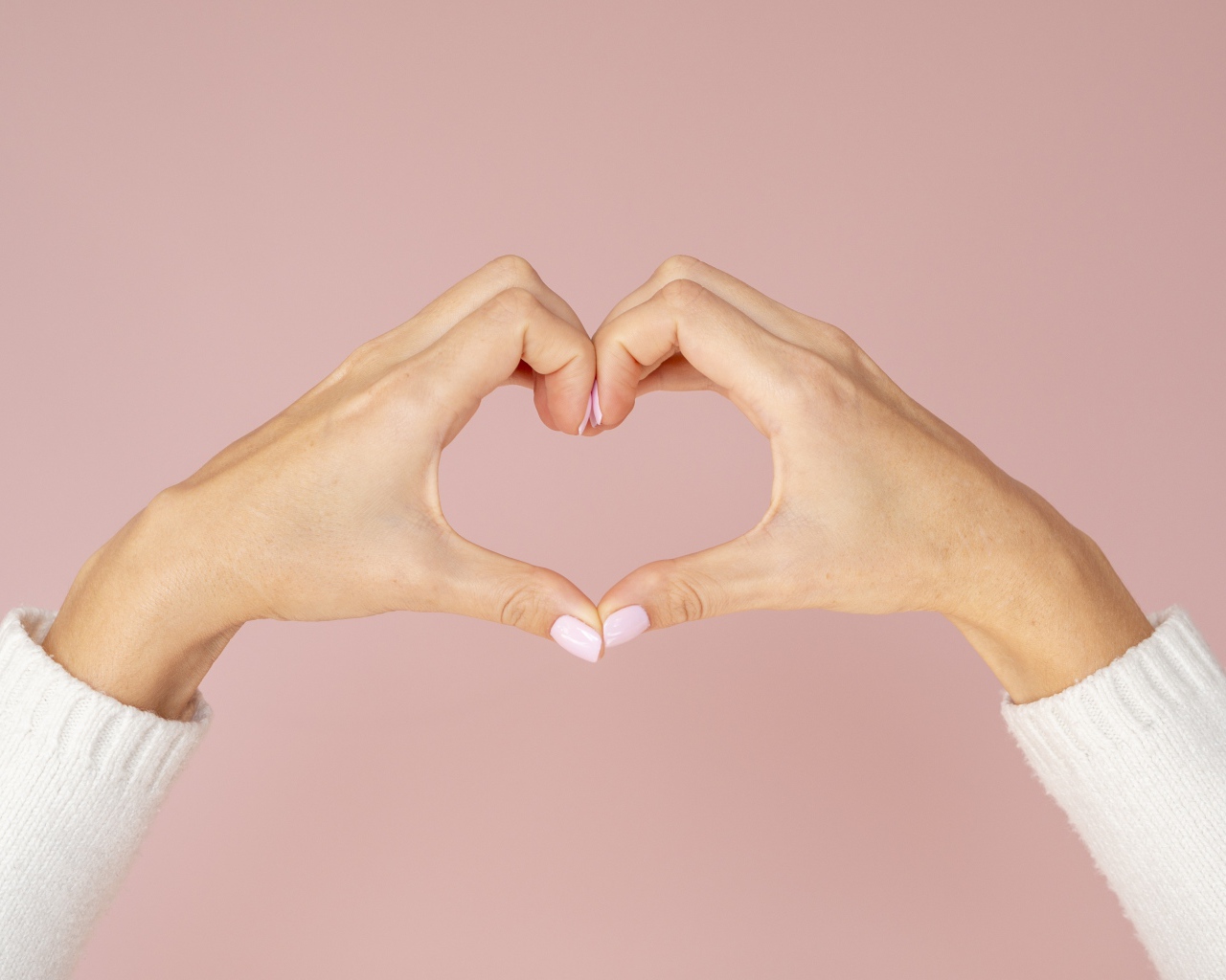 Девушка делает сердце руками на розовом фоне 