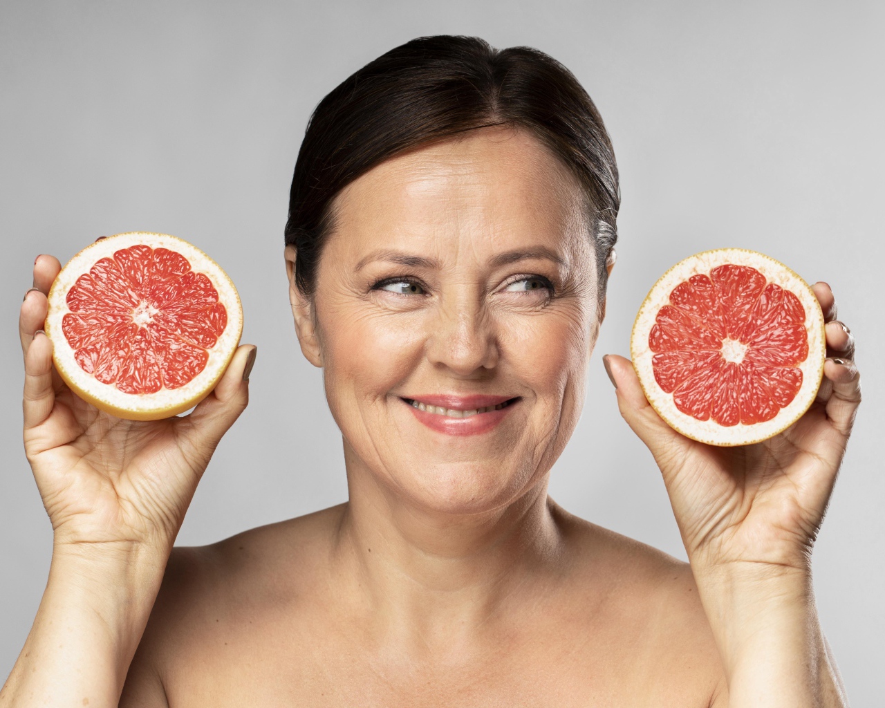 Улыбающаяся женщина с грепфрутом в руках на сером фоне