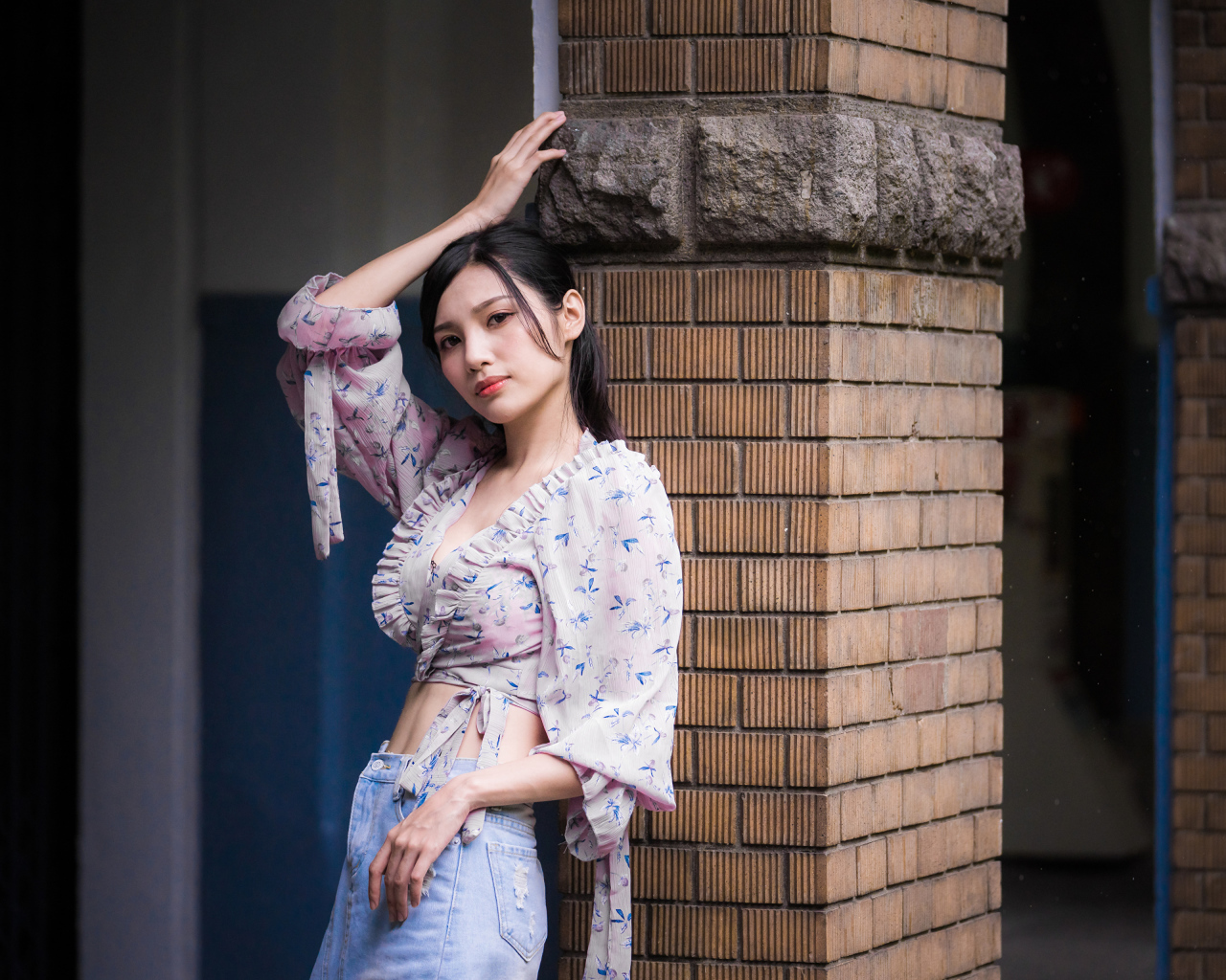 Красивая девушка азиатка стоит у кирпичной колонны 