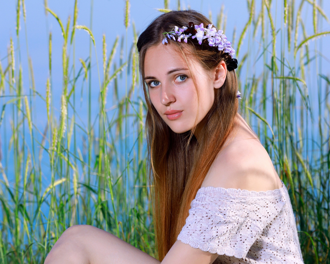 Красивая молодая девушка с венком на голове сидит на поле с колосьями 