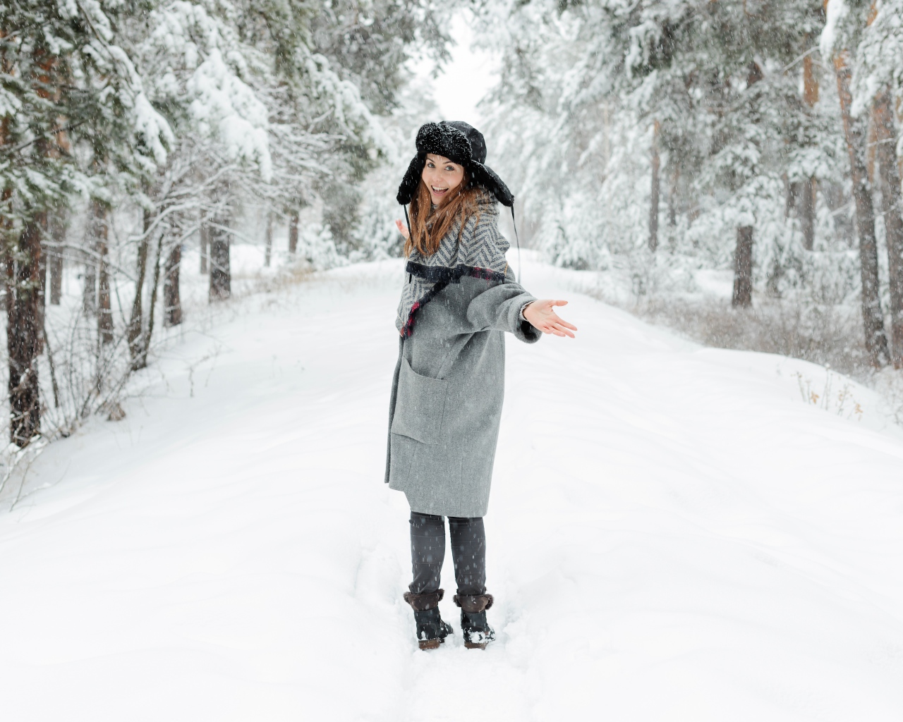 Девушка в пальто и теплой шапке гуляет в заснеженном лесу 