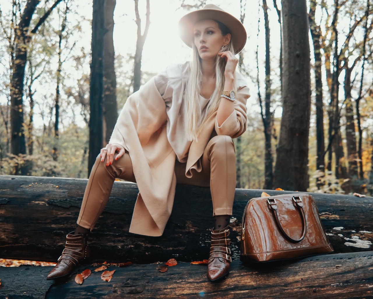 Девушка в пальто сидит на упавшем дереве в лесу 