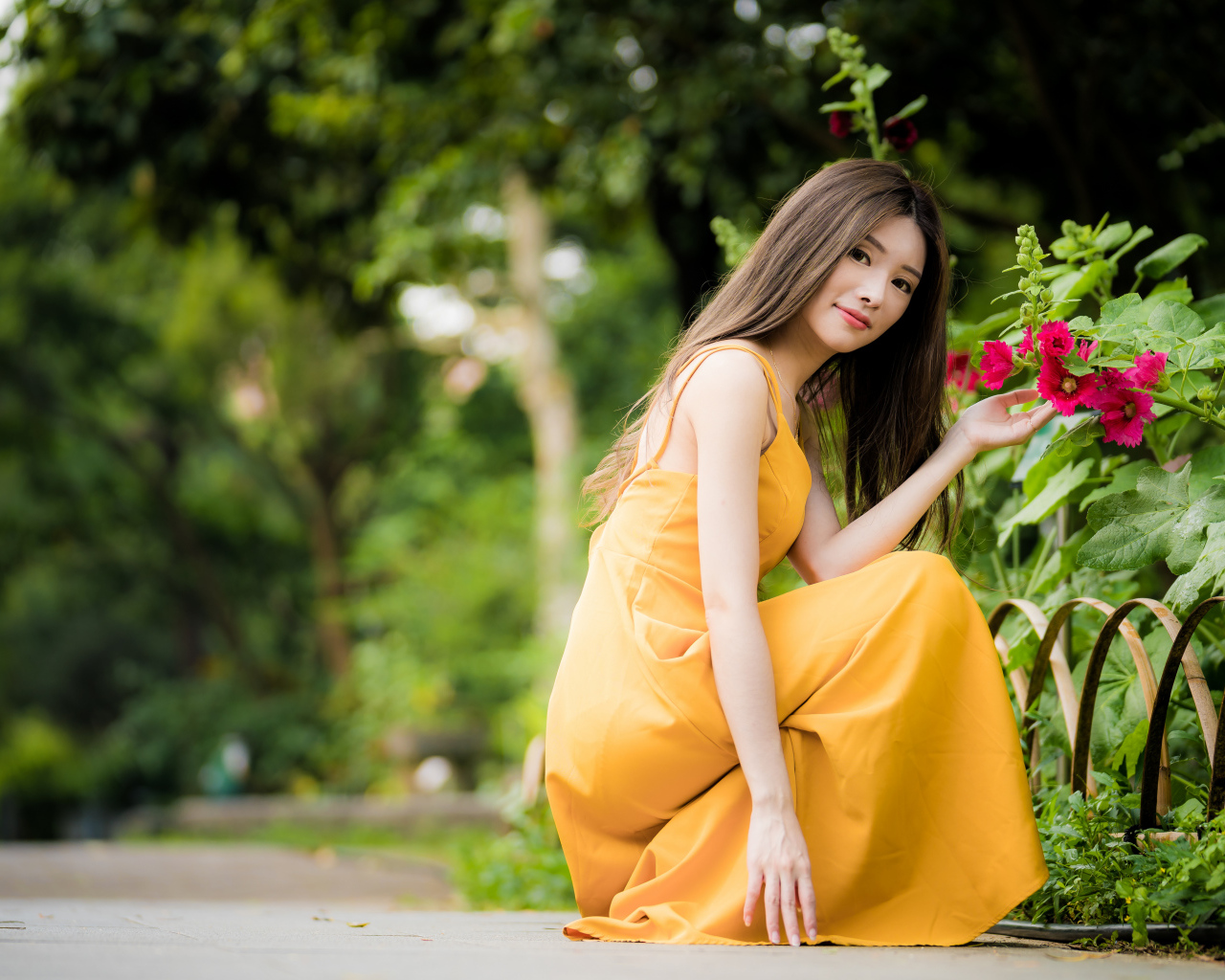 Девушка в желтом платье сидит у цветка мальвы в парке