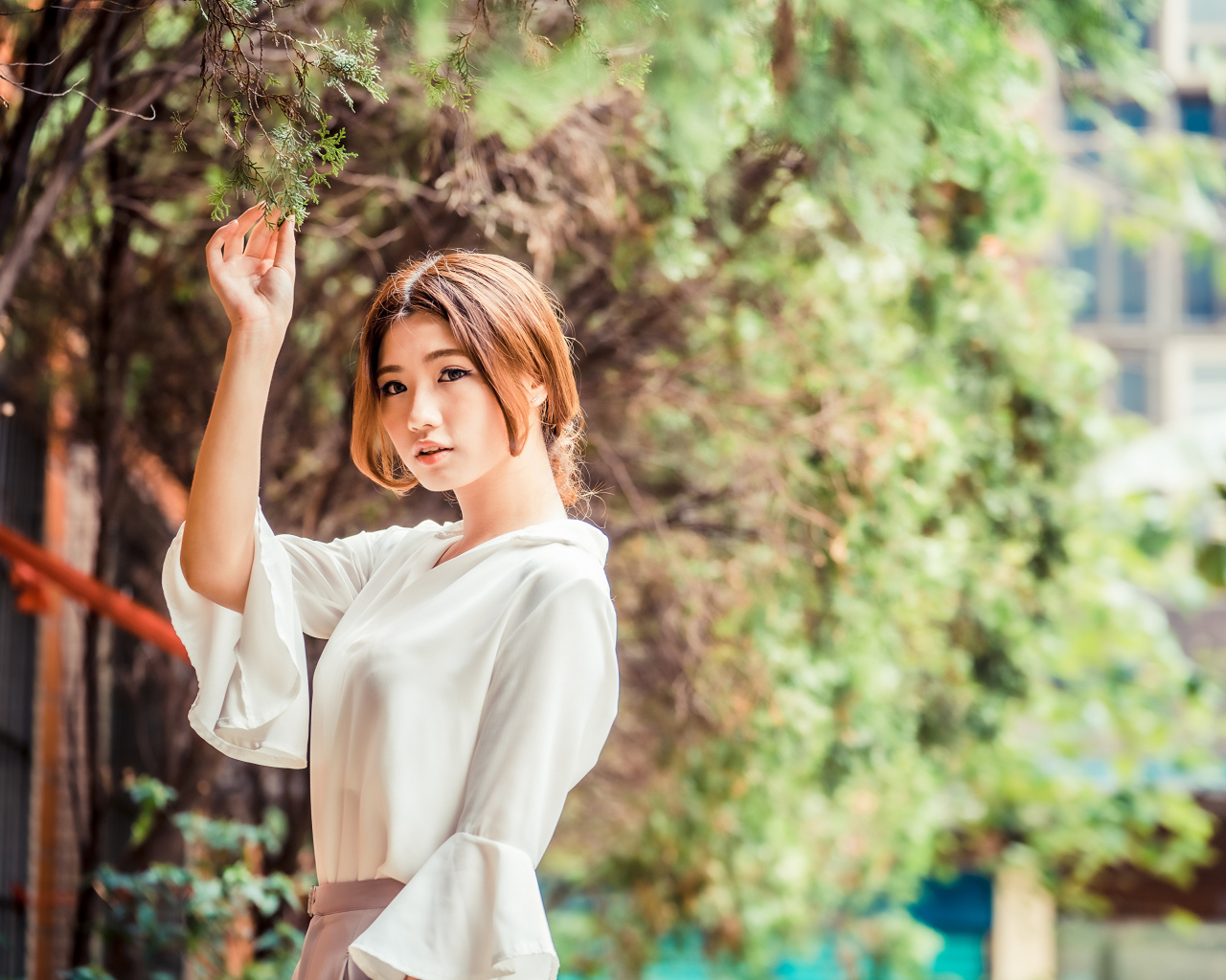 Молодая азиатка в белой блузке стоит у дерева 